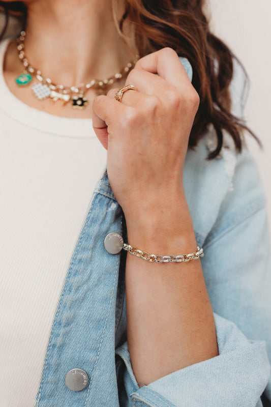 Close-up of a person wearing a bracelet, ring, and necklace with a light background