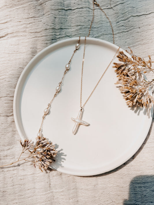 Necklace with a cross pendant on a white plate with dried flowers