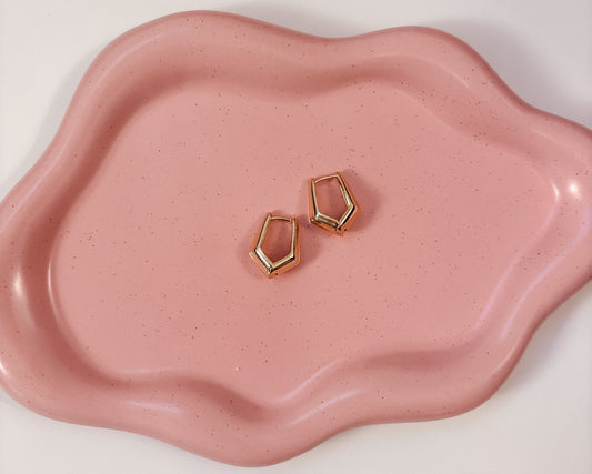 Gold geometric earrings on a pink ceramic dish
