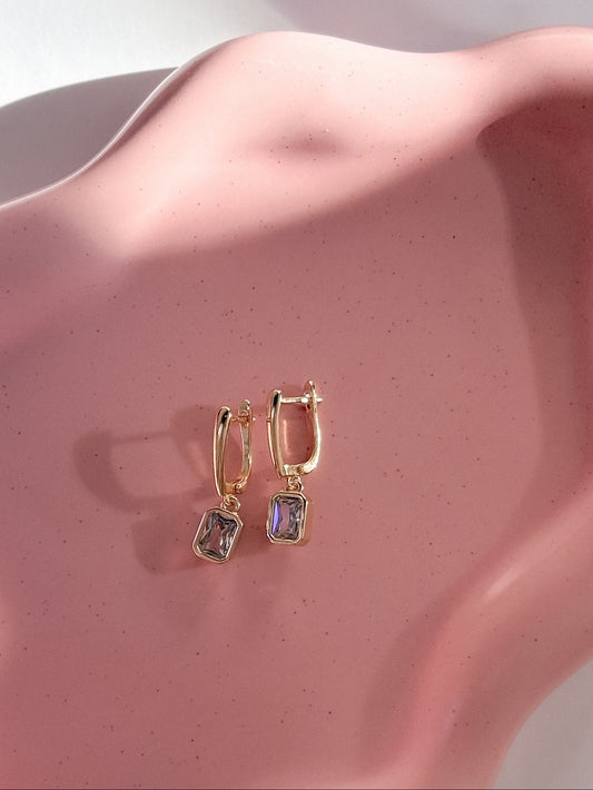 Pair of gold earrings on a pink wavy dish with a soft background