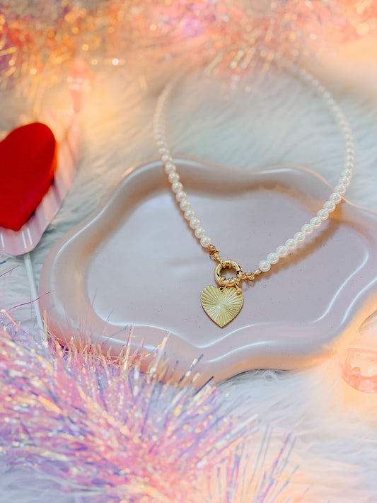 Pearl necklace with a gold heart pendant on a heart-shaped dish with a soft, blurred background.