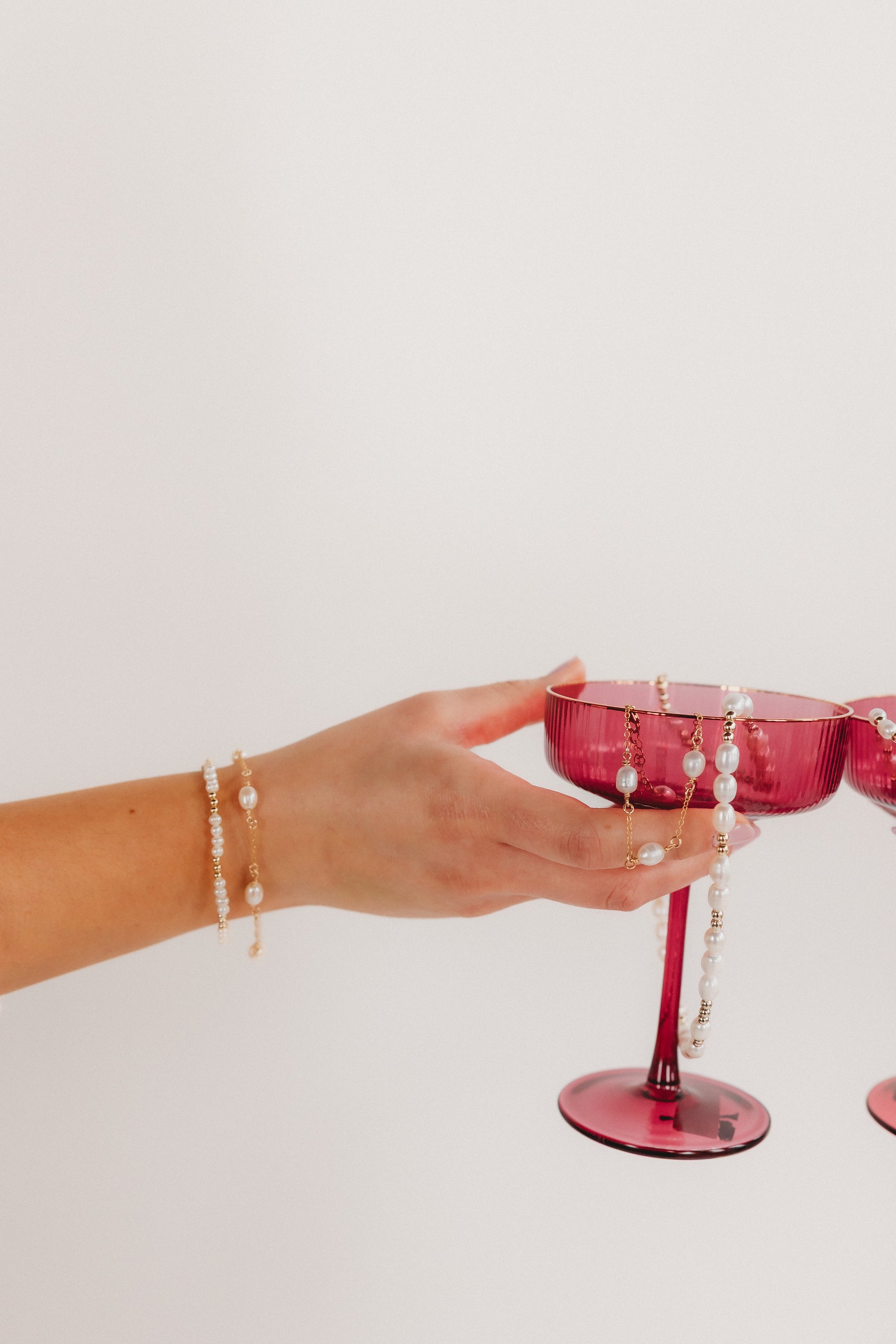Hand holding a pink glass with pearl decorations against a white background