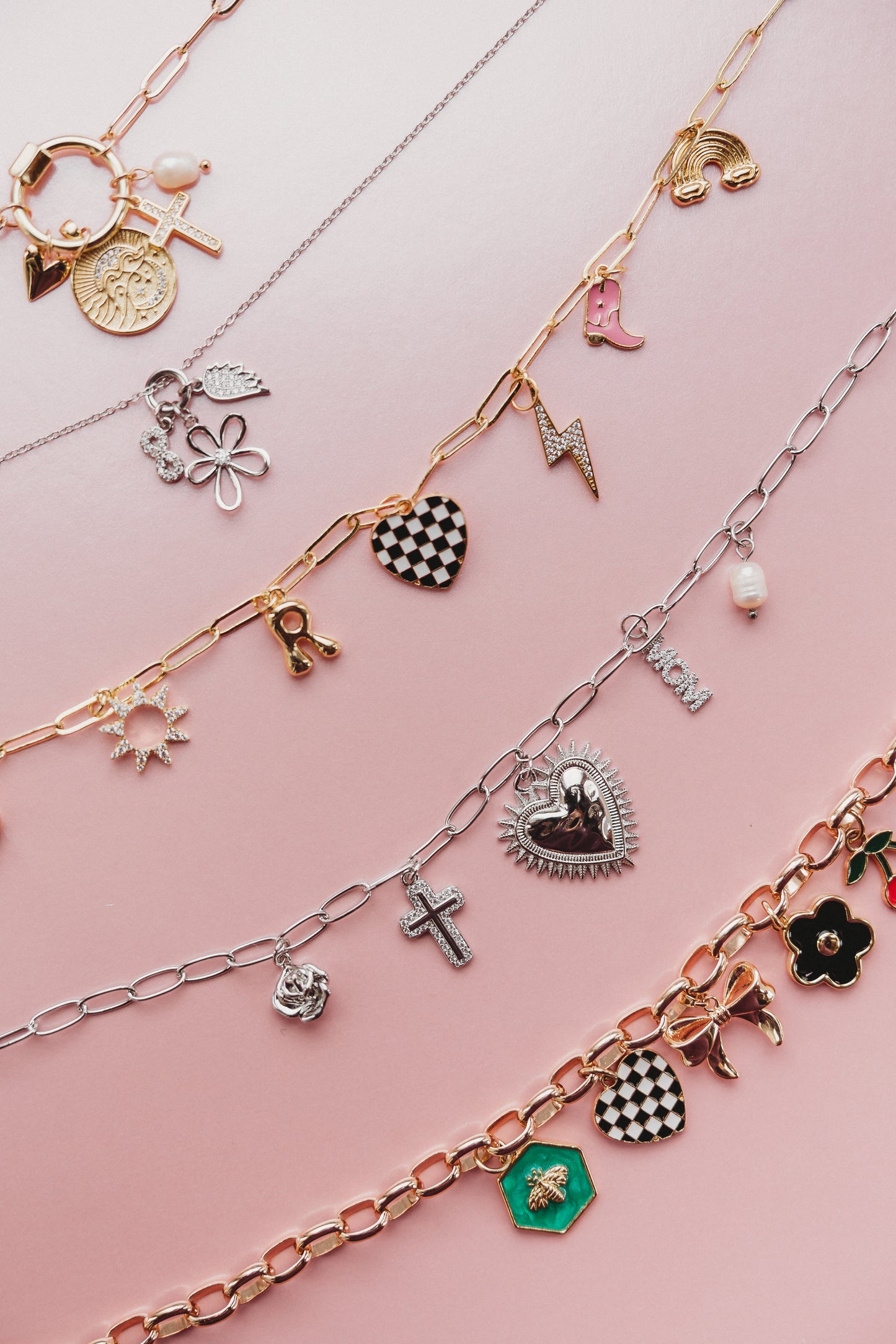 Multiple charm necklaces with various charms on a pink background