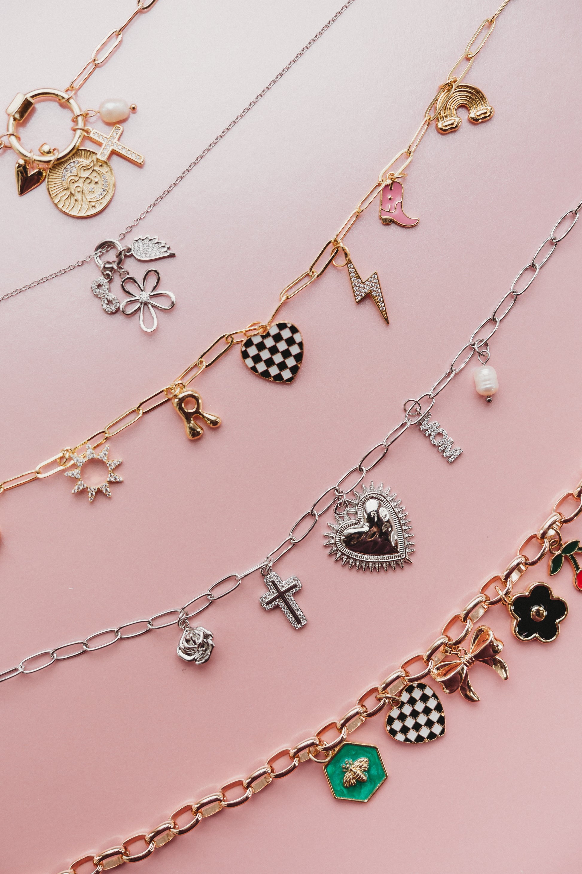 Multiple charm necklaces with various charms on a pink background