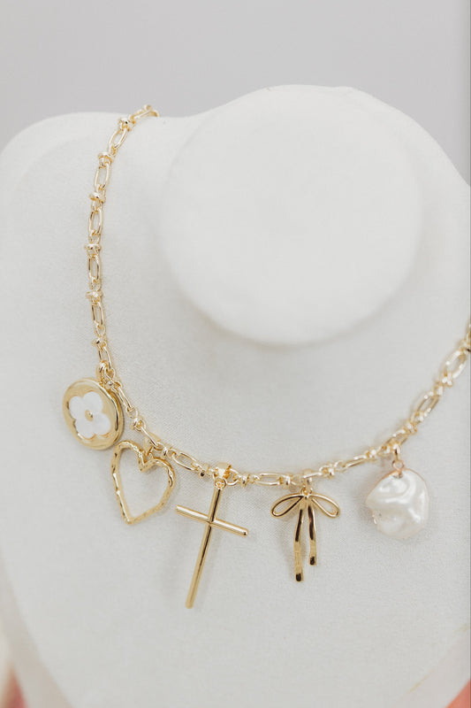Gold necklace with various charms on a white stand against a gray background