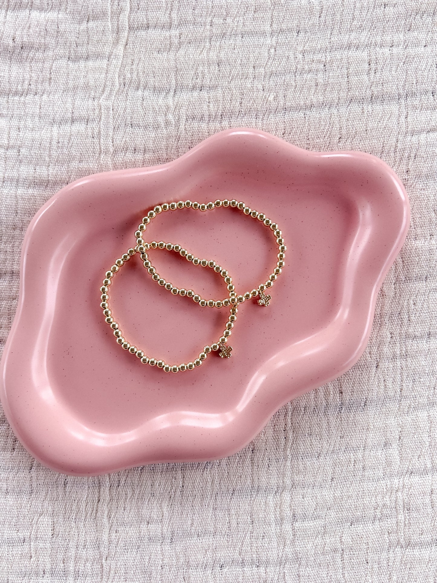 Pink jewelry dish with gold bracelets on a textured surface