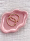 Pink jewelry dish with gold bracelets on a textured surface