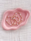 Pink ceramic dish with gold beaded white moonstone cross bracelets on a textured beige background