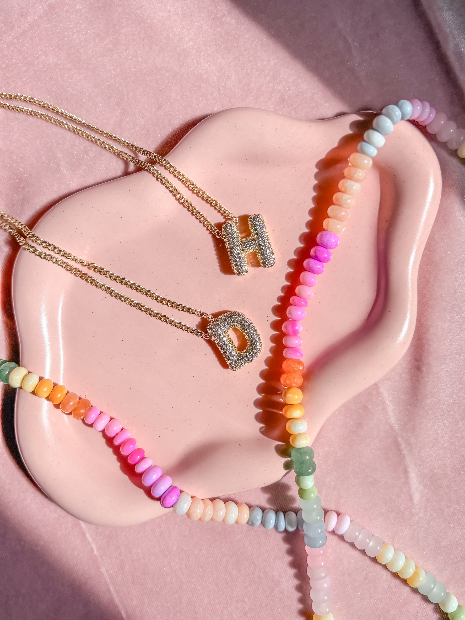 Necklaces with colorful beads and gold pendants on a pink mannequin bust.
