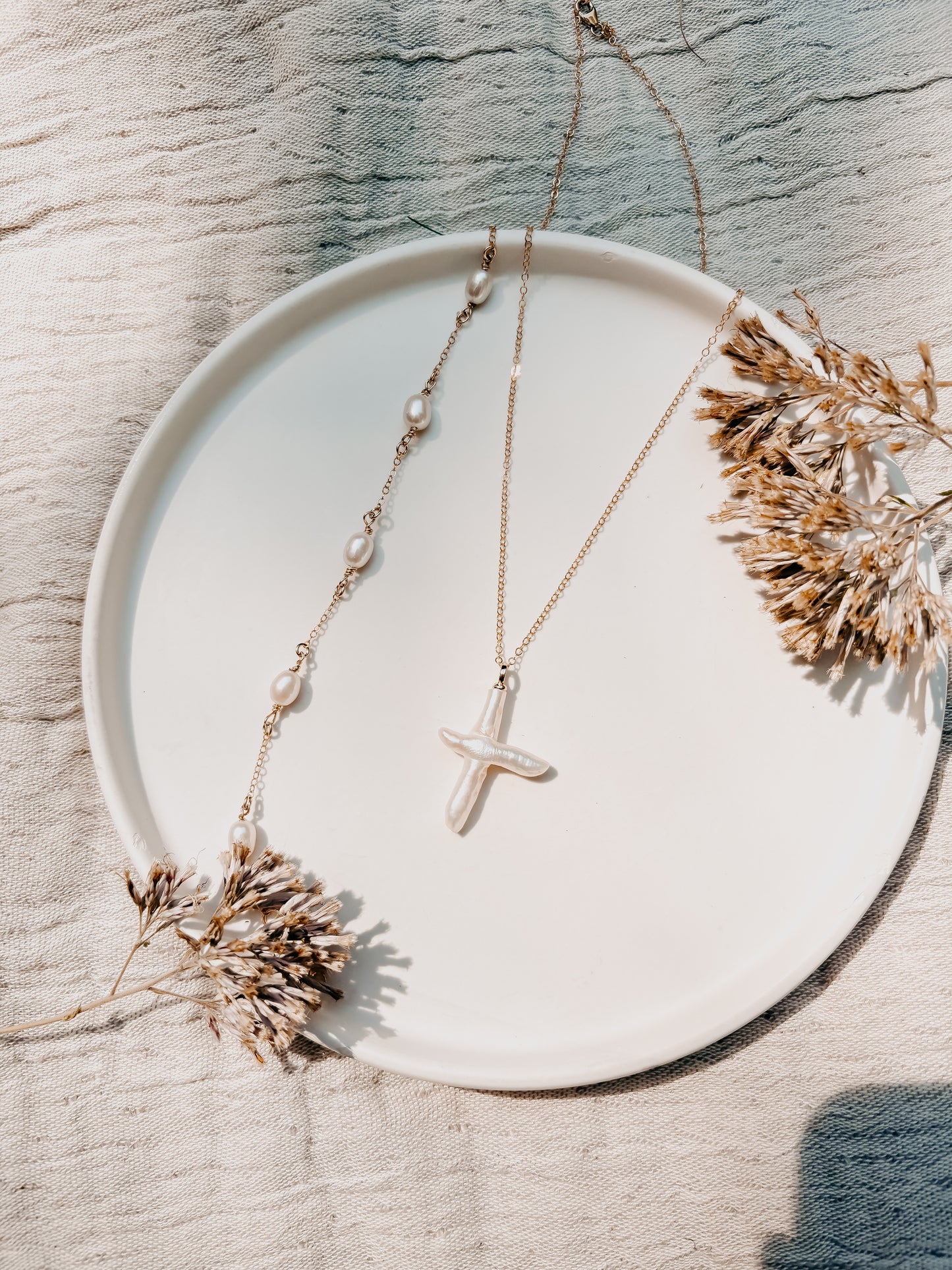 Necklace with a cross pendant on a white plate with dried flowers
