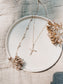 Necklace with a cross pendant on a white plate with dried flowers