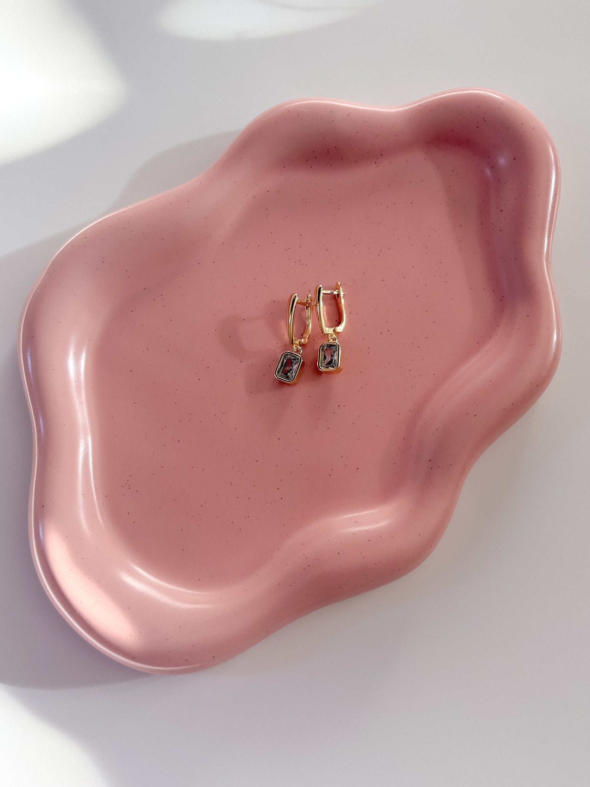 Gold hoop earrings on a pink ceramic dish with a white background