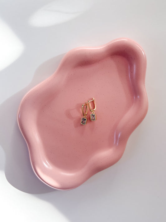 Pink ceramic dish with gold hoop earrings on a white background