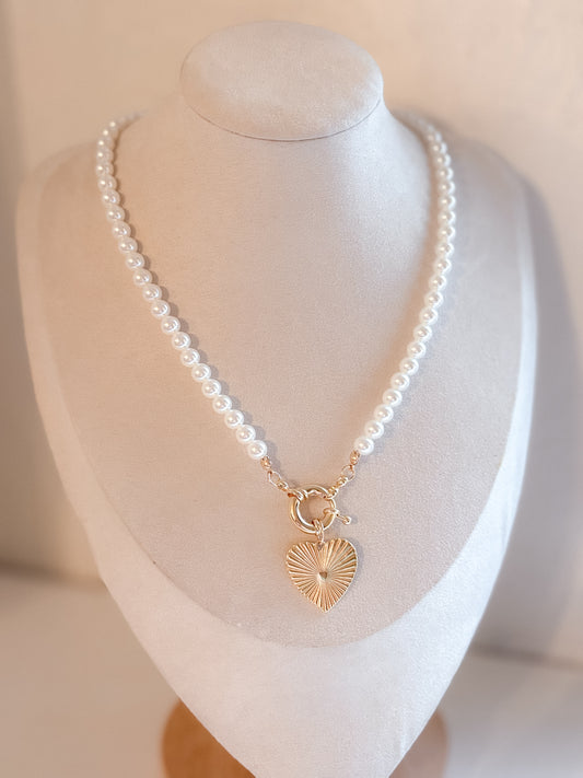 Pearl necklace with a gold heart pendant on a mannequin bust.