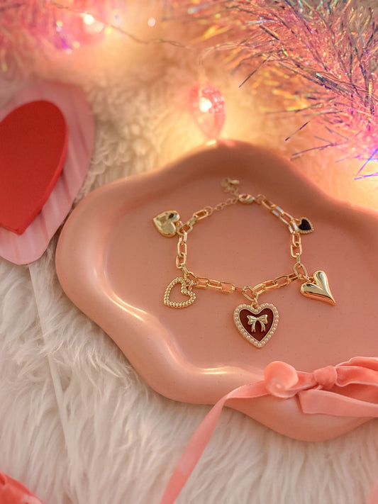 Gold bracelet with heart-shaped charms on a pink dish with a soft, blurred background