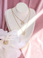 Gold necklaces with a 'D' and 'H' pendant on a mannequin bust with white flowers and pink background
