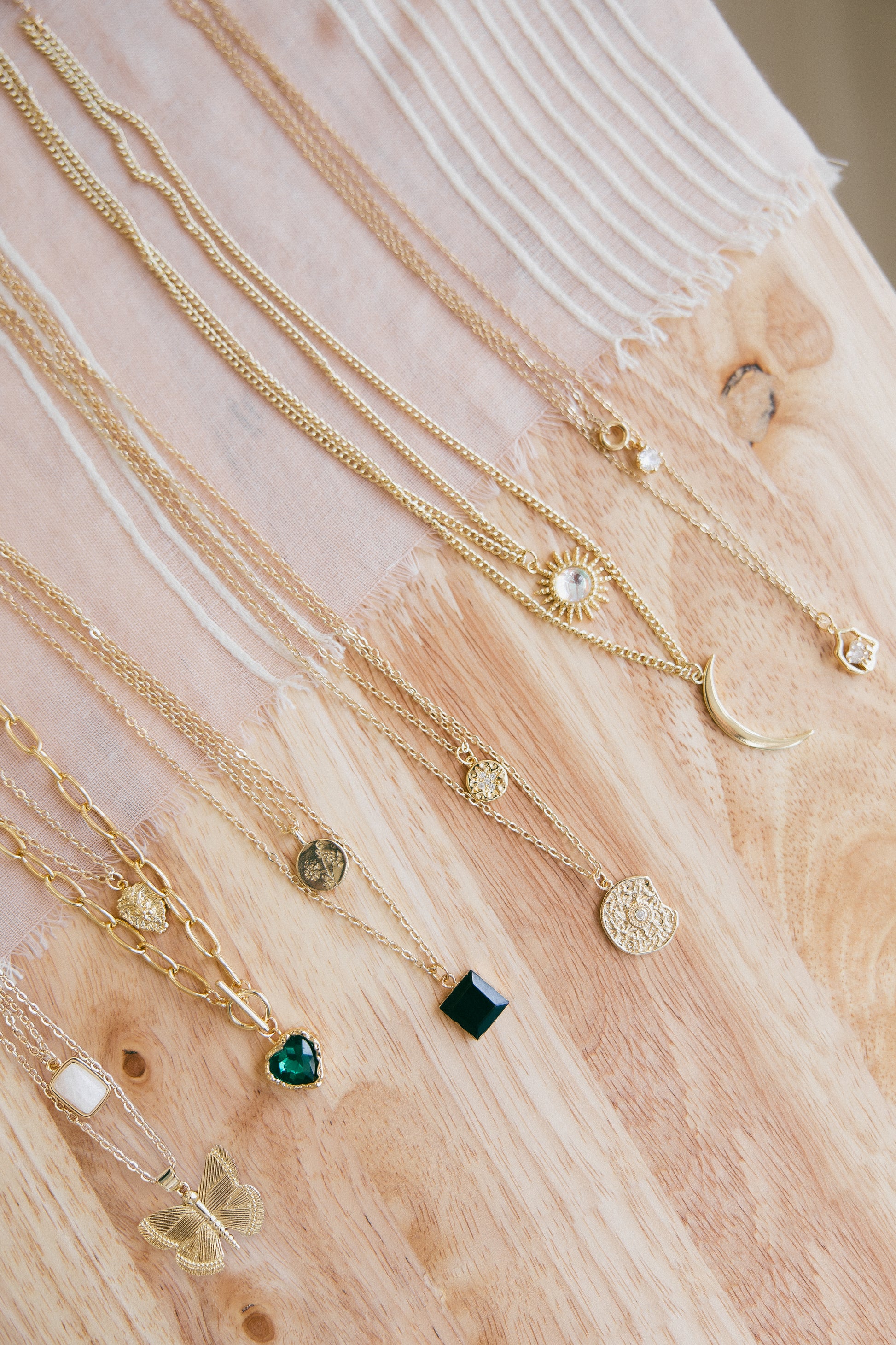 Gold necklaces with various pendants on a wooden surface